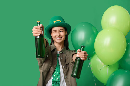 Beautiful young woman in leprechaun hat with bottles of beer and air balloons on green background. St. Patrick's Day celebration