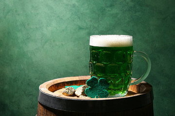 Glass of beer and clover on barrel against green background. St. Patrick's Day celebration