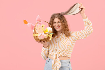 Beautiful young happy woman in bunny ears with Easter basket on pink background