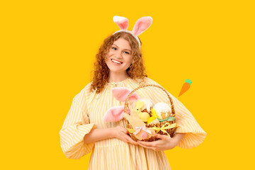 Beautiful young woman in bunny ears with Easter basket on yellow background