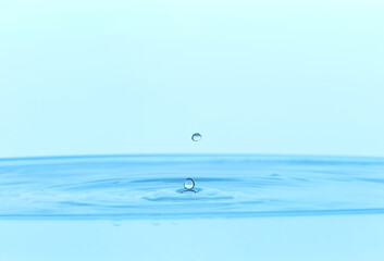 Drops falling into clear water on light blue background, closeup