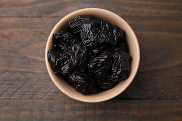 Sweet dried prunes in bowl on wooden table, top view