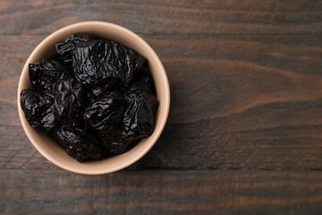 Sweet dried prunes in bowl on wooden table, top view. Space for text