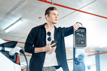 Young man travel with EV electric car to shopping center parking lot charging in downtown city...