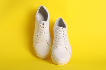 Pair of stylish white sneakers on yellow background