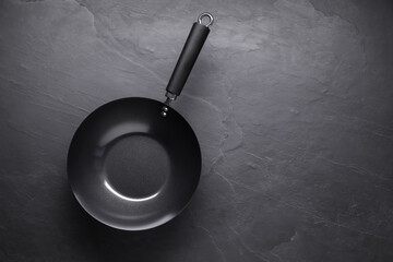 Empty iron wok on black textured table, top view. Space for text