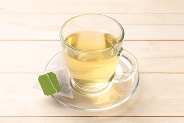 Tea bag and glass cup on light wooden table, closeup