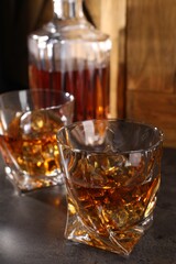 Whiskey with ice cubes in glasses and bottle on grey table, closeup