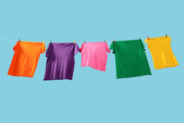 Colorful t-shirts drying on washing line against light blue background, low angle view