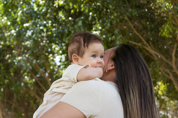 Bebé cargado por su mamá en un parque rodeado de árboles en un día soleado