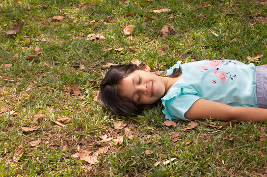Ni&ntilde;a sonriendo de siete a&ntilde;os echada sobre el pasto en el parque en un d&iacute;a soleado rodeada de naturaleza y hojas de los &aacute;rboles