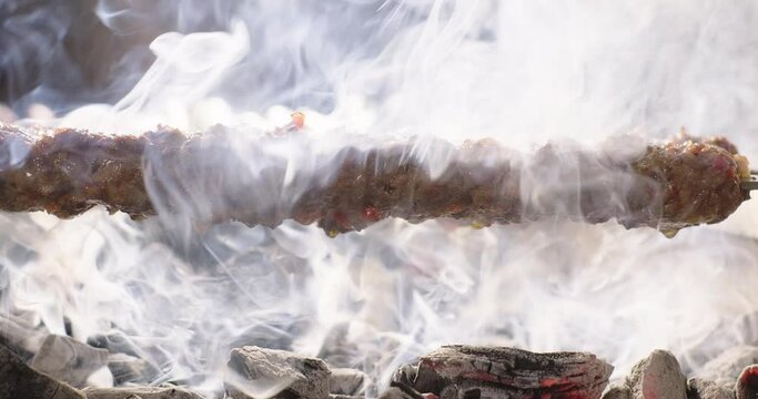 Adana kebab barbecue on charcoal grill. Meat juice dripping on charcoals. Traditional Turkish kebab grilled on skewers. Close-up