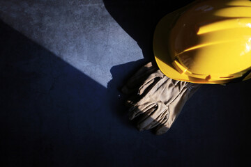 industrial worker theme with the sun shines down on leather gloves and a yellow safety hat on a black background, copy space for placing text on the left - obrazy, fototapety, plakaty