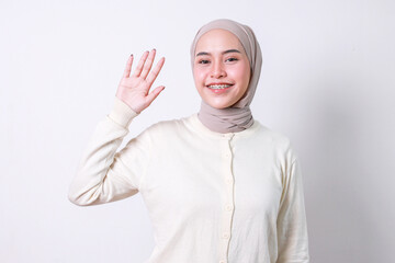 Asian muslim woman with braces teeth waving hand say hi or goodbye over white background