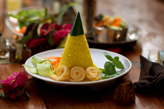 Nasi Tumpeng Mini or Nasi Kuning. Yellow rice in a cone shape. A festive Indonesian rice dish with side dishes.