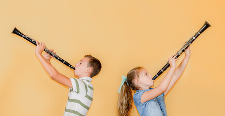 A boy and a girl with clarinets are standing with their backs to each other, playing the clarinet,...
