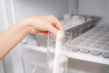 The girl collects frozen ice cubes from the freezer to prepare soft drinks.