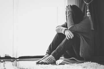 Monochrome shot of depressed woman sitting alone in living room caused of sadness or broken heart.