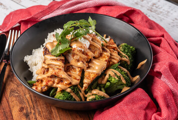 A top-down view of a bowl of Peri Peri Chicken in a round bowl with broccoli, with rice and spicy sauce