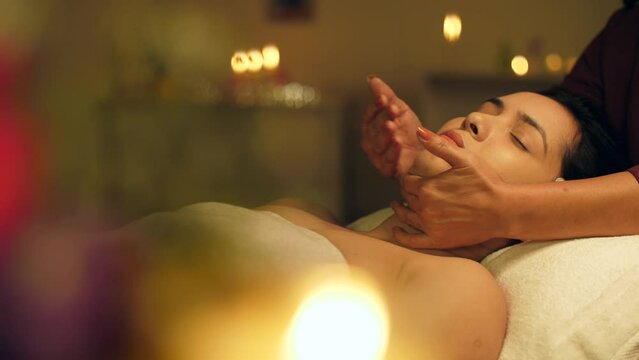 A young Asian woman receiving a body massage in a spa center - spa treatments  relaxing neck massage. Shot of an Indian girl relaxing during neck and shoulder massage lying on a massage table - Rel...