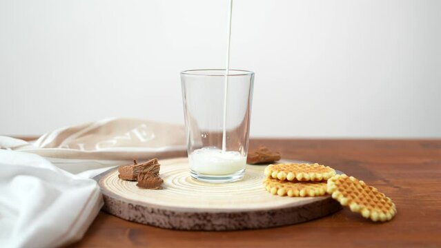 Milk is poured into a glass on a wooden table with biscuits next to it