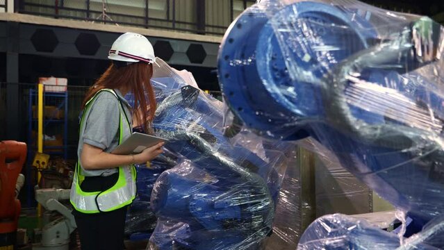 Female engineer walking around carefully inspecting the new robot zone in the warehouse robot is covered clear dustproof plastic sealed and the robot inspection service is waiting electrical testing.