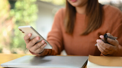 Closeup view female hands holding smartphone with blank empty display and credit card