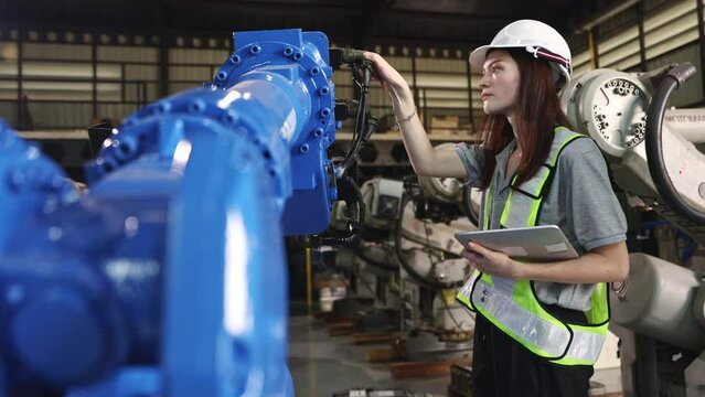 Caucasian female electronics engineer holding laptop Inspect automation electrical wiring connections and electrical connections industrial robots operating with modern technology in the warehouse.