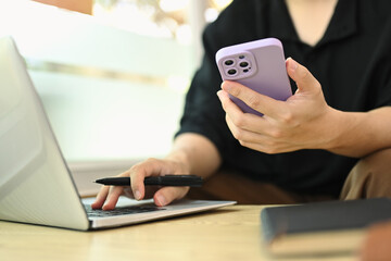 Young man freelancer holding mobile phone and working on laptop at cafe
