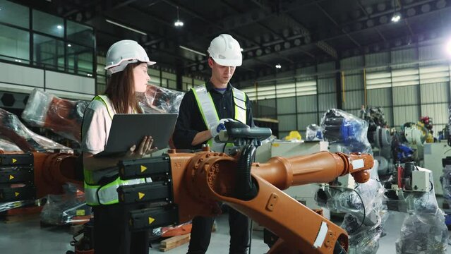 Male and female electrician robot engineer inspecting new welding robot testing electrical installation process with laptop electronic automation system setup in warehouse modern business industry 4.0