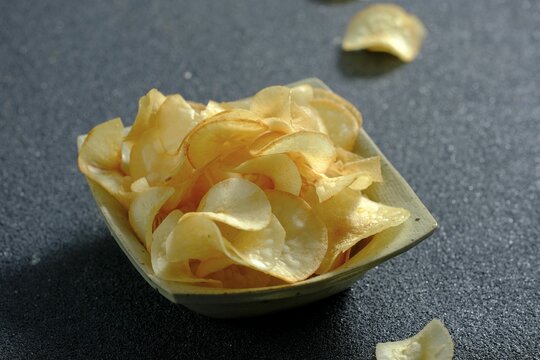 Criping, fried cassava chips in square bowl with black background. Crunchy and savoury taste. Kripik singkong