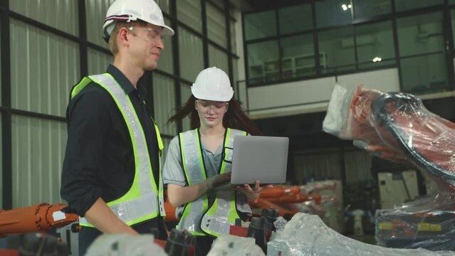 Male and female robotics engineers inspect new robot zone robot warehouse covered in clear dustproof plastic and an inspection service with laptop robots are waiting for electrical testing.