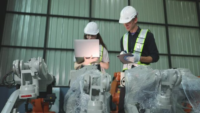 Male and female robotics engineers inspect new robot zone robot warehouse covered in clear dustproof plastic and an inspection service with laptop robots are waiting for electrical testing.