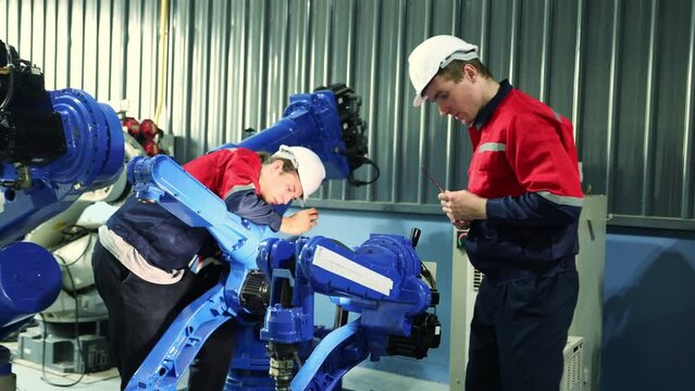 Team male engineer technicians work safely helping to check the structural integrity of electric welding robot arm assemblies in the maintenance shop using phillips screwdriver with dexterity.
