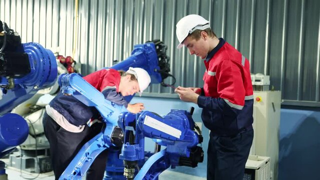 Team male engineer technicians work safely helping to check the structural integrity of electric welding robot arm assemblies in the maintenance shop using phillips screwdriver with dexterity.
