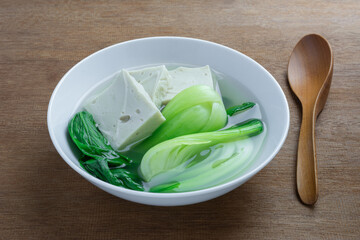 close up view of bok choy soup with bean tofu in a ceramic bowl on wooden table. asian homemade style food concept.