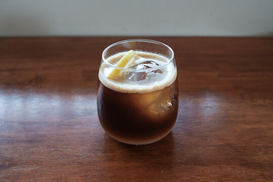 a lemon juice iced coffee and lemon slices in a glass on a wooden table with natural light