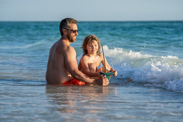 Fototapeta premium summer vacation of friendly family dream. Son and father playing in summer sea. Father and son on sea. Exploring sea with a toy ship as father and son. Creating summer memories
