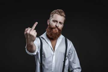 Vintage brutality guy showing middle finger in retro suspenders. Retro man in suspenders isolated on black. Mature redhead man with hairstyle. Vintage male fashion style. Male vintage style