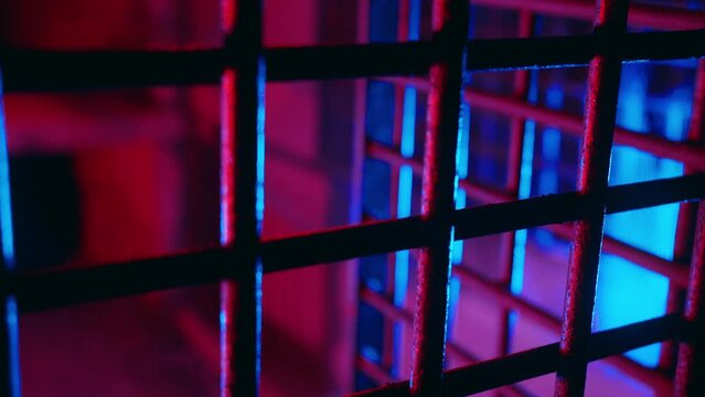 Cinematic metal bars in scary dungeon cell for torture. Abandoned prison. Creepy cage underground. Thriller jail lit with ambient red and blue neon light. Ancient underground chamber. Old prison grate