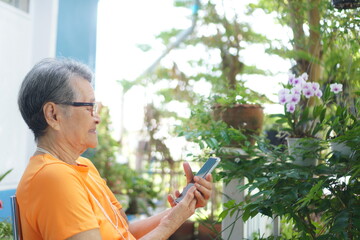 Asian grandmother wearing eyeglasses uses a smart phone to contact her family happily ,  Relaxed...