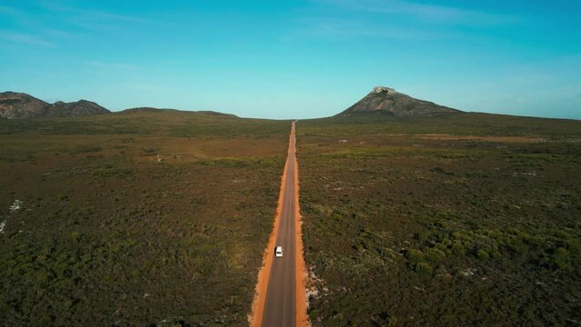 aerial of a van driving on a straight road in Cape Legrand National Park in Western Australia with frenchman peak in the background on a sunny day