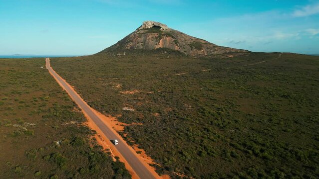 van driving on a straight road in cape legrand national park with frenchman peak in the background on a sunny day, esperance, western australia