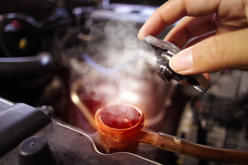 Auto mechanic hand opens the radiator cap with steam escaping around the engine compartment from...