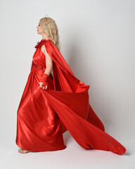 Full length portrait of beautiful blonde model dressed as ancient mythological fantasy goddess in flowing red silk toga gown, crown.   Walking away from camera,  isolated on white studio background. - obrazy, fototapety, plakaty