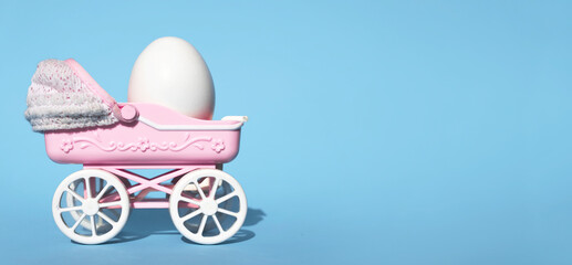 Chicken egg in toy miniature crib on blue background. Easter celebration concept.  Place for text.