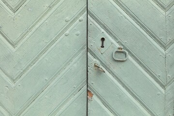 Closeup of keyhole and handle on a light green painted wood door.