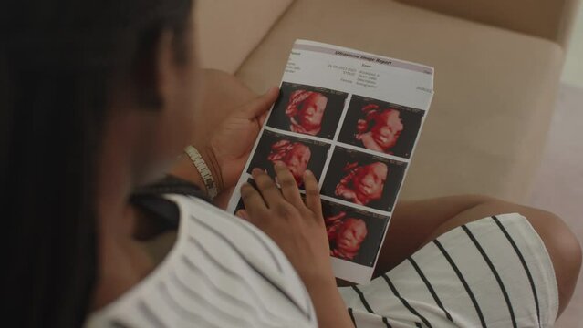 Over the shoulder view of future African American mother looking at ultrasound image of her baby at home