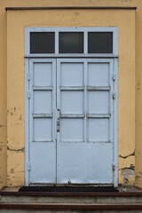 Fototapeta na wymiar Grey painted metal door with windows on top on a yellow painted stone building.