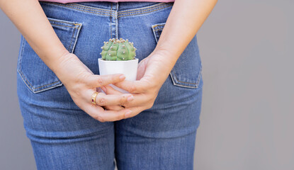 Back view of young woman with cactus standing over light gray background. Hemorrhoids concept